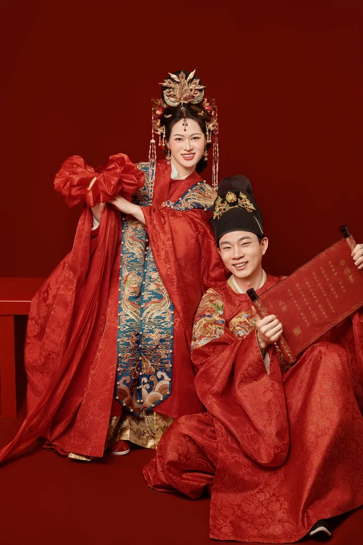 两人手持红绸与书帖,轻松欢笑的中式婚照